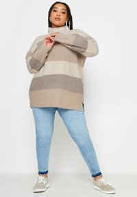 Sweter dziany w beżowe i jasnobrązowe paski, z wysokim kołnierzem, długimi rękawami i bocznymi rozcięciami. Połączony z jasnoniebieskimi dżinsami skinny i szarymi trampkami.
