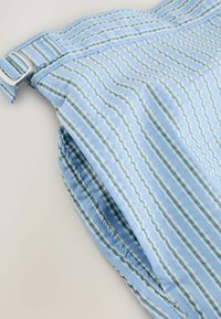 Világoskék textil rövidnadrág, amelyen függőleges csíkok találhatók különböző kék és zöld árnyalatokban, ezüst csattal a derekán.