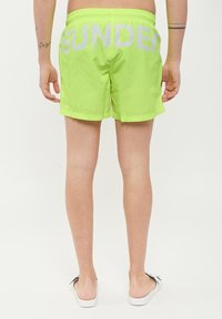 Pantaloni da bagno verde neon con vita elasticizzata. Stampa "SUNDAY" in grandi lettere bianche riflettenti sul retro. Tessuto liscio e leggero.