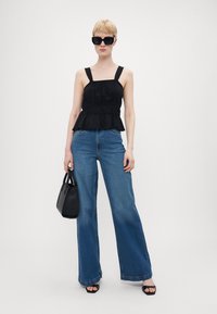 Svart peplum-top med brede stropper, kombinert med lyseblå, høy midje jeans. Modellen holder en svart veske og har på seg oversized solbriller.