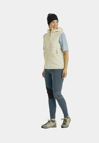 Leichte Daunensteppweste mit Kapuze, seitlichen Taschen und Reißverschluss. Getragen über einem kurzärmlichen hellblauen Oberteil und dunkelblauen Hosen mit schwarzen Akzenten.