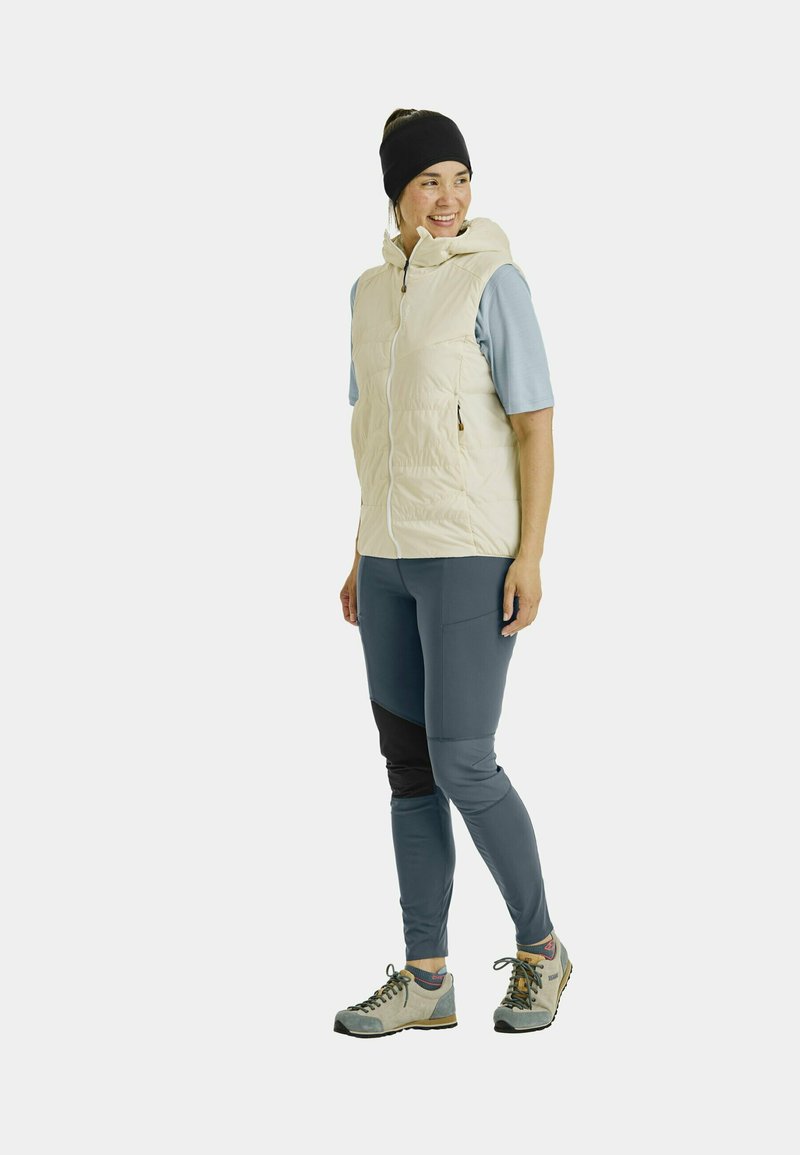 Leichte Daunensteppweste mit Kapuze, seitlichen Taschen und Reißverschluss. Getragen über einem kurzärmlichen hellblauen Oberteil und dunkelblauen Hosen mit schwarzen Akzenten.