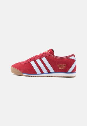 Czerwony but sportowy Adidas z białymi paskami, gumową podeszwą i złotym napisem "Adidas Italia" po boku, widoczny od wewnętrznej strony.