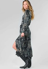 Lang zwart kledingstuk met een paisleypatroon, een tailleband en lange mouwen. Draagt met zwarte kniehoogte laarzen met gespen. Gladde textuur.