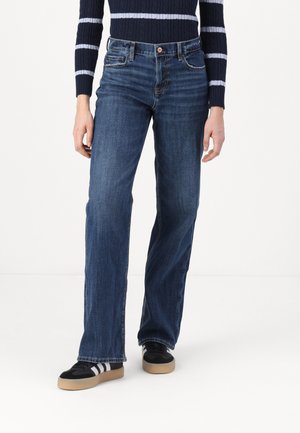 Dark blue denim jeans with a straight-leg cut, featuring front pockets and subtle stitching details, paired with black sneakers.