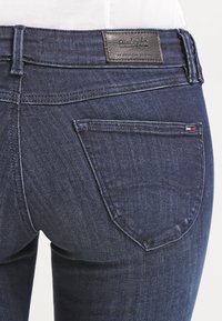 Jeans de mezclilla azul oscuro con una textura suave, un diseño de bolsillo trasero y una etiqueta de cuero con marca en la cinturilla.