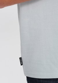 T-shirt in cotone grigio chiaro con etichetta laterale che presenta la scritta "LEVEL UP." Tessuto morbido e maniche corte, indossato con jeans di denim scuro.