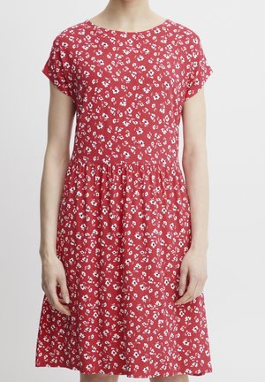 Femme portant une robe rouge à manches courtes avec un petit imprimé floral blanc et noir, taille froncée et encolure ronde.