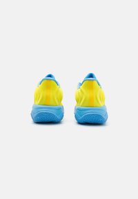 Lys gule atletiske sko med en blå sål og detaljer. Har en struktureret overdel med en glat finish og et buet hældesign.
