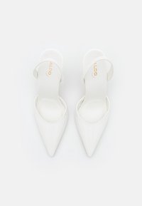 Bílé lakované kožené lodičky na klínku s špičatou špičkou a tenkým nártem. Vyznačují se elegantní siluetou a hladkým povrchem.