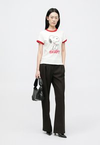 Vit T-shirt med röd ringer-halsringning, med en Snoopy-grafik och text. Matchad med svarta byxor med vida ben och en svart texturerad handväska.