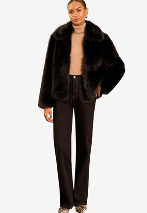Giacca di pelliccia ecologica nera con un ampio colletto, abbinata a un dolcevita beige e a jeans neri a vita alta. Scarpe con stampa animale completano il look.