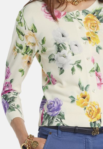 Krém színű virágos kardigán, rózsaszín, sárga, lila és fehér virágokkal díszítve. Puha anyagú, gombos záródású, háromnegyedes ujjú, bordázott szegéllyel.
