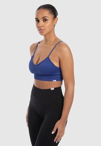 Bralette azul con relieve y tirantes finos, con un diseño de escote en v, combinado con leggings negros de cintura alta. Textura suave, con un branding mínimo visible.