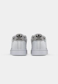 Pair of white Adidas sneakers shown from the back, featuring gray heel tab with black Adidas logo and stitching details.