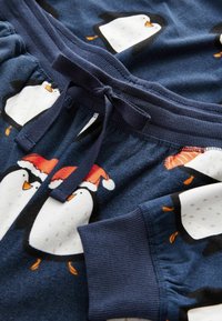 Pimeä siniset pyjamashortsit, jotka on valmistettu pehmeästä kankaasta ja joissa on pingviinikuosi, jossa on joulupukkihattuja. Sisältää nauhavyötärön ja ribbaustaskut.