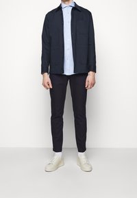 Granatowa krótka kurtka na jasnoniebieskiej koszuli na guziki, w połączeniu z ciemnymi spodniami i kremowymi trampkami. Prosty fason z kieszeniami na kurtce.