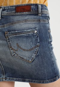 Jeanskjol i medelblå färg med en urtvättad finish. Har en prissatt läderlapp, bakfickor och kontrasterande sömdetaljer.