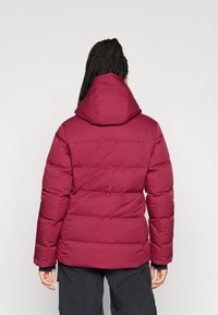 Veste rembourrée bourgogne avec capuche, présentant un design matelassé et des poignets élastiques, fabriquée en matériau synthétique, vue de dos.