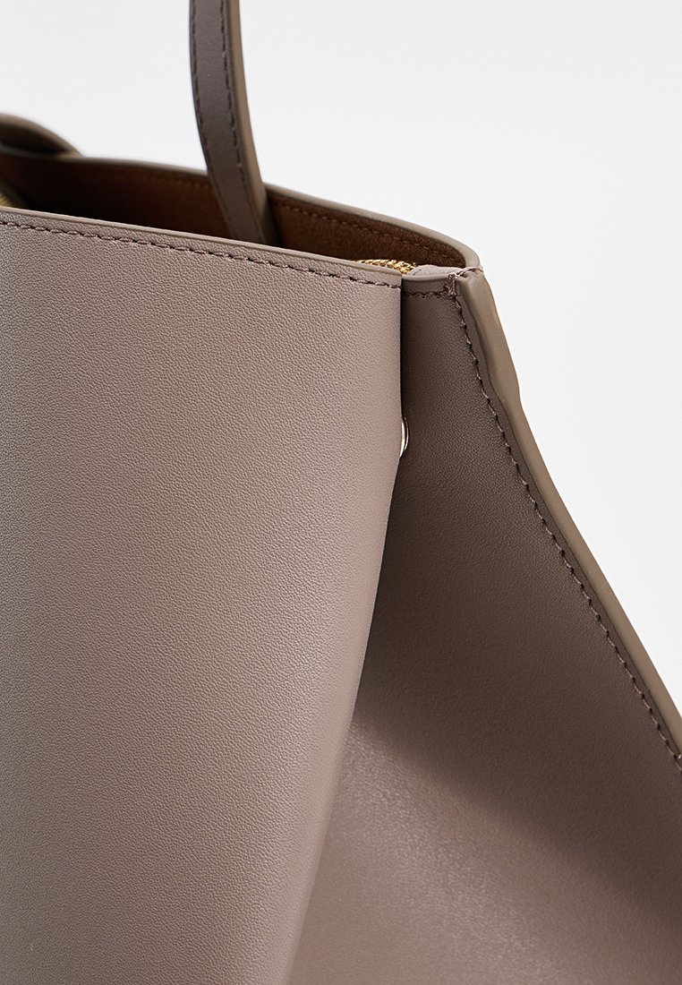 Grau Leder Shopper mit glatter Textur und strukturiertem Design. Verfügt über einen goldenen Reißverschluss und eine teilweise offene Oberseite für einfachen Zugang.
