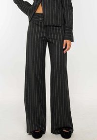 Pantalones de traje gris a rayas con un corte ajustado, que presentan una pierna ancha, cierre de botón y un ligero brillo en la tela.