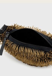 Čierna taška so zlatými kovovými hrotmi po obvode, vybavená zipsovým otvorom a hladkým vnútrom. Rukoväte vyrobené z kože.