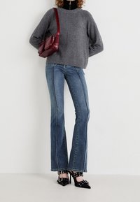 Szary dziergany sweter, rozszerzane niebieskie dżinsy z kontrastowym przeszyciem i czarne szpilki z akcentami ze srebrnego metalu.