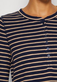 Granatowo-beżowa koszulka henley z długim rękawem w paski, z okrągłym dekoltem i pięcioma guzikami z przodu. Miękka, prążkowana tekstura.