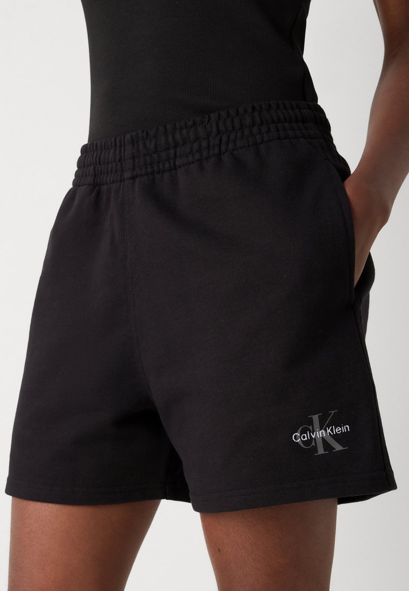 Zwarte katoenen shorts met een elastische tailleband, zijzakken en een klein grijs "Calvin Klein" logo op het linkerpijp. Eenvoudig, casual ontwerp.