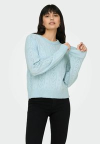 Pull tricoté bleu clair avec un motif chevron, poignets et ourlet côtelés. Le matériau semble doux avec une épaisseur moyenne.