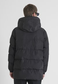 Giacca a vento nera con cappuccio. Design trapuntato e imbottitura spessa per isolazione. Presenta una texture liscia e lucida e polsini a coste.