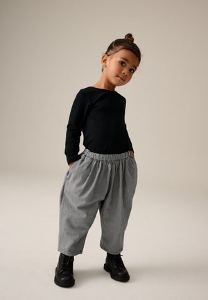 Schwarzes Langarmoberteil, graue und schwarze karierten Baggy-Hosen mit elastischem Bund und schwarzen Schnürstiefeletten. Einfaches, lässiges Outfit.