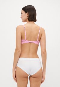 Rosa spets-bh med justerbara band, prydd med en scalloped kant; ihop med enkla vita högmidjade underkläder, med slät yta.