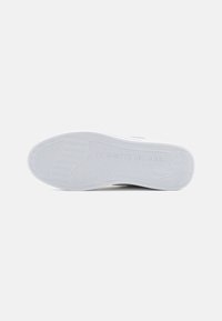 Suola di sneaker bianca in gomma con una superficie testurizzata, inclusi scanalature e un logo, caratterizzata da un design classico a profilo basso.