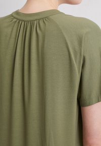 Olijfgroen korte mouw top met een ronde halslijn. De achterkant heeft plooien voor extra textuur en een iets losse pasvorm. Zachte stof.