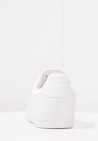 White leather sneaker with a smooth texture, rounded heel, and rubber sole featuring a subtle pattern. No visible branding on the back.