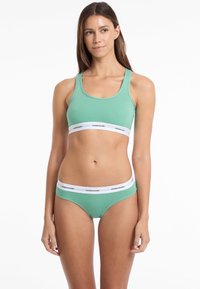 Mintgroen beha- en bikini-set van gladde stof, met witte elastische banden met het logo "GUESS JEANS" op de taille.