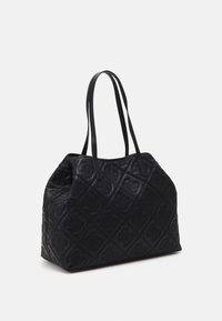 Sac cabas matelassé noir avec motifs floraux en relief et deux fines bretelles sur un fond clair uni.