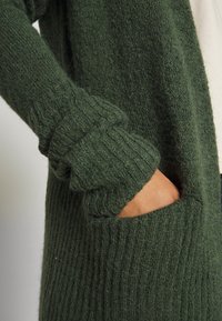 Světle zelený pletený cardigan s ribovanými manžetami a kapsami, s měkkým, texturovaným povrchem.