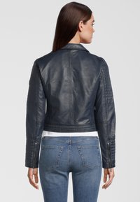 Veste cropped en cuir marine avec des détails matelassés aux épaules, des poignets zippés et une silhouette ajustée. Texture lisse et design de col accentué.