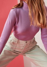 Col roulé côtelé violet associé à un pantalon taille haute vert menthe avec fermeture à boutons et effilochage sur les côtés de l'ourlet.