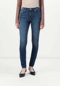 Donkerblauwe skinny jeans van denim, met een klassiek vijf-pocket ontwerp en een hoge taille. Gecombineerd met zwarte puntige ballerina's.