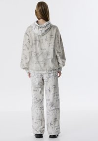 Haut à capuche oversize gris clair et pantalon large, tous deux ornés de motifs de texte manuscrit noir. Tissu doux avec une coupe décontractée.