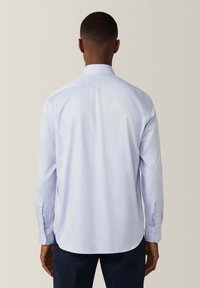 Camisa de botones azul claro hecha de tela texturizada, con mangas largas, cuello puntiagudo y dobladillo curvado.