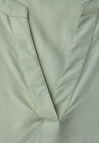 Gros plan sur un tissu vert clair avec un détail de couture en forme de V au centre.