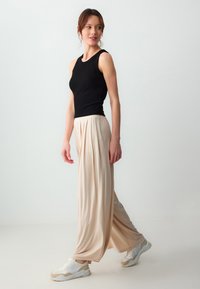 Zwart mouwloos topje, beige geplooide wijde broek, gladde textuur, zachte val, gecombineerd met witte en beige sportieve sneakers.