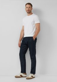 Maglietta in cotone bianca, pantaloni plettati blu navy e sneakers crema con dettagli marroni. Design semplice, vestibilità comoda, stile casual.