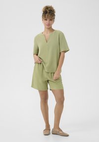 Lichtgroene casual outfit met een T-shirt met korte mouwen en een V-hals, en bijpassende shorts, gemaakt van geweven stof. Eenvoudig ontwerp en pasvorm.