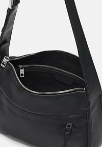 Bolso de mano de cuero negro con correa ajustable, compartimento principal con cremallera y bolsillo interior adicional. Textura suave con herrajes en tono plateado.