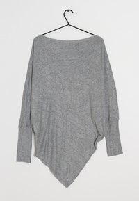Haut oversize à manches longues gris clair avec un large décolleté et un ourlet asymétrique pointu. Le tissu semble doux avec une finition légèrement texturée.